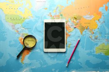 Tablet computer, pencil and magnifier on world map�