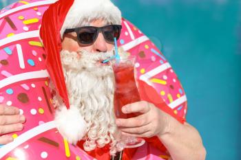 Santa Claus with inflatable ring and cocktail near swimming pool at resort�