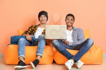 Portrait of young students with laptop sitting near color wall�