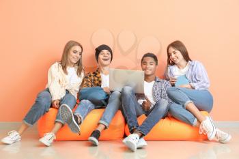 Portrait of young students with laptop sitting near color wall�