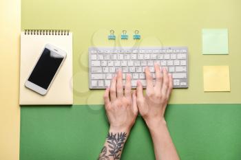 Female hands with PC keyboard, mobile phone and stationery on color background�