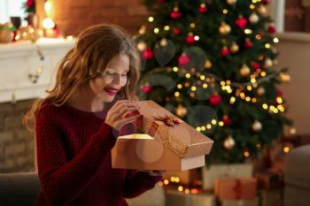 Happy young woman opening Christmas gift at home�