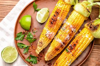 Plate with tasty grilled corn cobs on table�