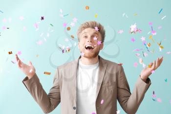 Happy young man and falling confetti on color background�