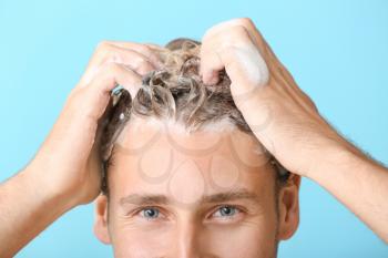 Handsome young man washing hair against color background, closeup�