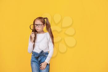 Little girl with magnifying glass on color background�