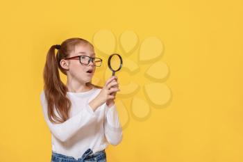 Surprised little girl with magnifying glass on color background�