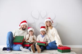 Happy family with Christmas gifts sitting near light wall�