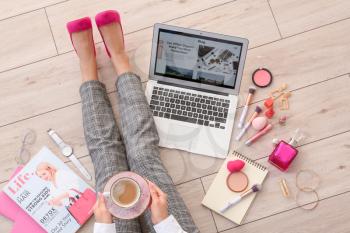 Female beauty blogger with laptop and cup of coffee sitting on wooden floor, top view�