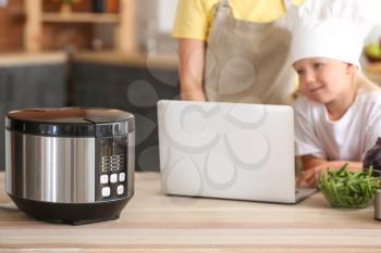 Woman and her little daughter with laptop and modern multi cooker in kitchen�