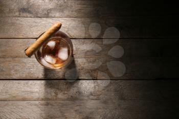 Glass of cold whiskey with cigar on wooden table�