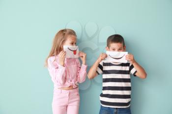 Little children hiding mouths behind drawn smiles on color background�