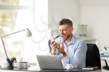 Stressed man talking by mobile phone at table in office�