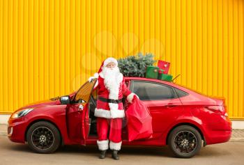 Santa Claus with gifts in bag getting out of car outdoors�