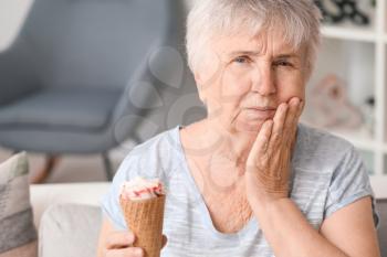 Senior woman with sensitive teeth and cold ice-cream at home�