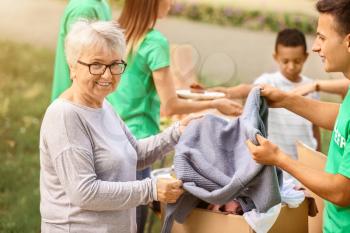 Young volunteer giving new clothes for poor senior woman outdoors�