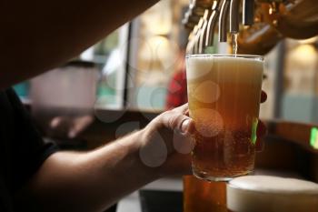 Barman pouring fresh beer in glass, closeup�