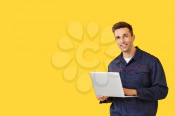 Male car mechanic with laptop on color background�