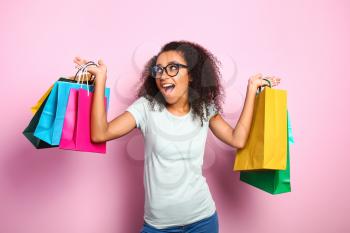 Portrait of happy African-American woman with shopping bags on color background�