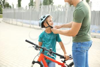 Father helping his son to put on helmet before riding bicycle outdoors�