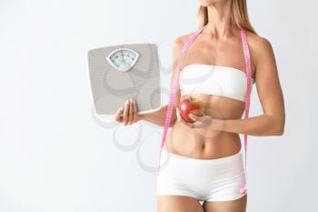 Beautiful young woman with measuring tape, scales and apple on light background. Weight loss concept�