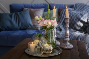 Beautiful burning candles with flowers on wooden table in room�