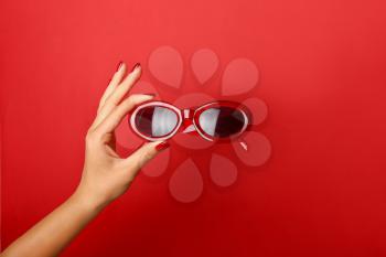 Female hand with stylish sunglasses on color background�
