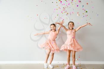 Portrait of happy twin girls with falling confetti near light wall�