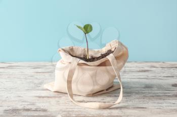 Eco bag with soil and plant on wooden table against color background�