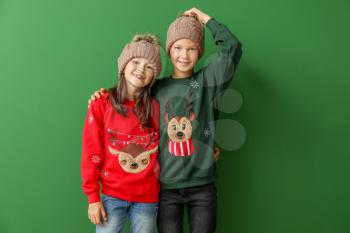 Little children in Christmas sweaters and knitted hats on color background�