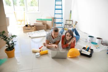 Happy young couple with laptop planning repair in their new house�