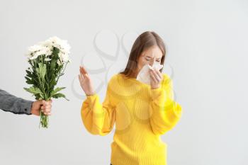 Young woman with allergy refusing to take flowers from man on light background�