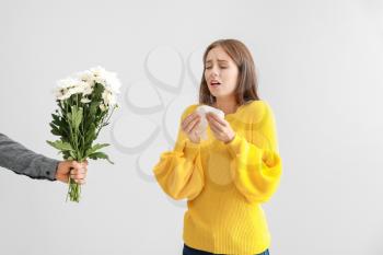 Man giving flowers to young woman suffering from allergy on light background�