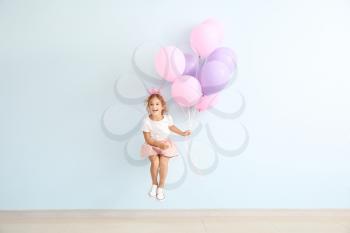 Jumping little girl with balloons on color background�