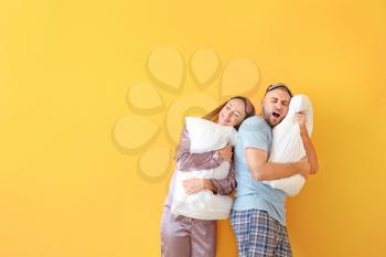 Sleepy young couple with pillows on color background�