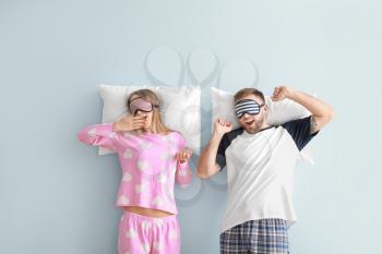 Sleepy young couple with pillows on color background�