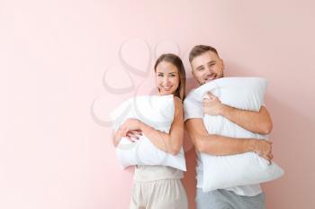 Young couple with pillows on color background�