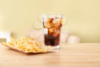 Glass of cold cola and french fries on table�