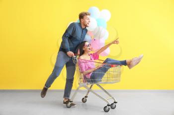 Young couple with shopping cart and balloons near color wall�