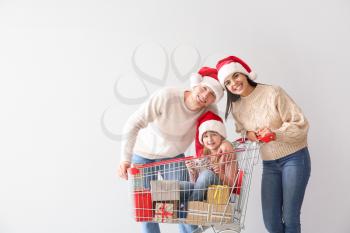 Family with shopping cart full of Christmas gifts on light background�
