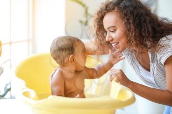 Young African-American mother washing her baby at home�
