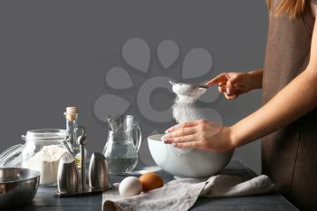 Woman sieving flour in kitchen�