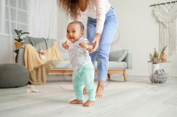 African-American mother teaching her little baby to walk at home�