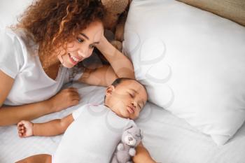 Young African-American woman and her sleeping baby on bed�