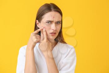 Portrait of young woman with acne problem squishing pimples on color background�
