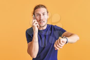 Stressed man talking by phone while looking at watch on color background�