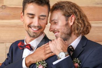 Portrait of happy gay couple on their wedding day against wooden background�