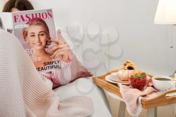 Woman reading fashion magazine before breakfast in bedroom�
