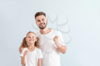 Portrait of father and his little daughter with toothbrushes on light background�