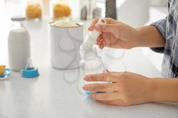 Woman preparing baby milk formula at table in kitchen�